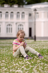 A girl sits in a meadow of flowers and smells a flower