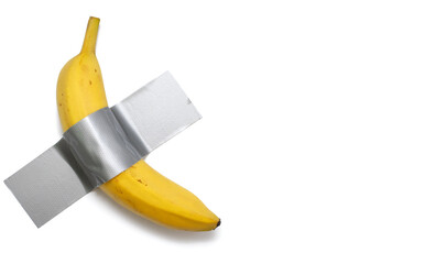 A banana is taped to a white wall with gray tape. A conceptual look at contemporary art. Ripe banana glued to a white isolated background. Free space for text and ads