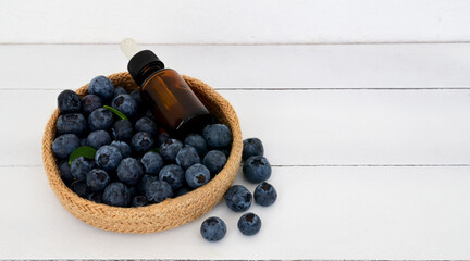 Blueberry seed essential oil in a glass bottle and fresh blueberries on a white wooden background.Healthy  natural cosmetics,spa and body care concept with copy space.Selective focus.
