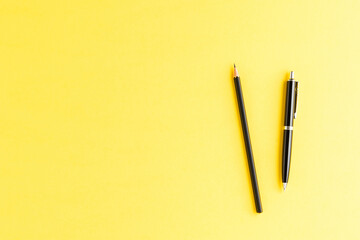Office desktop with black pen and pencil on yellow background. Top view