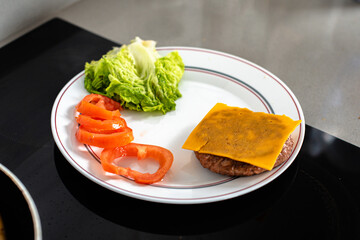Un plato que contiene los diferentes ingredientes para confeccionar una hamburguesa: carne, queso, lechuga y tomate - obrazy, fototapety, plakaty