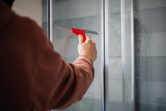 Un hombre limpiando la mampara de la ducha con una rasqueta de silicona. Concepto de limpiacristales. Herramienta para limpiar los vidrios