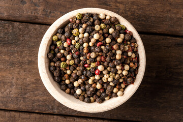 Mixed peppercorns in bowl on wooden table. Close up. Top view