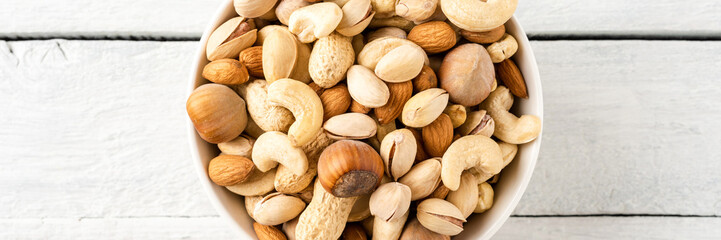 Mixed dried nuts (almonds, pistachios, peanuts, hazelnuts and cashews) in bowl on wooden table. Top...