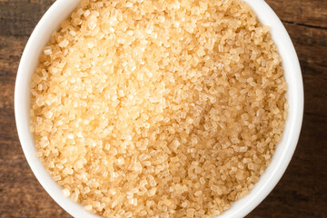 Brown cane sugar in bowl on rustic wooden table. Top view
