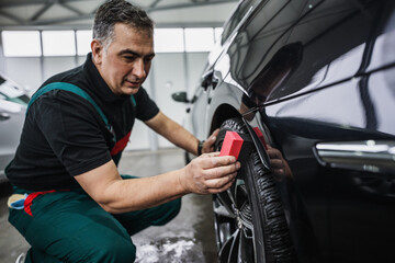 Professional car service worker polishing luxury car rim with microfiber rag or cloth in a car detailing and valeting shop. Ultra wide angle shot.