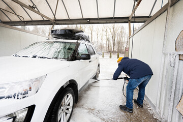 Man washing high pressure water american SUV car with roof rack at self service wash in cold weather.