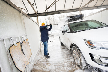 Man washing high pressure water american SUV car with roof rack at self service wash in cold weather.