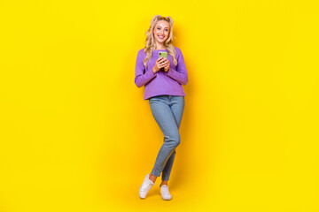 Fototapeta na wymiar Full length photo of lovely young lady hold telephone typing reading news dressed stylish violet look isolated on yellow color background