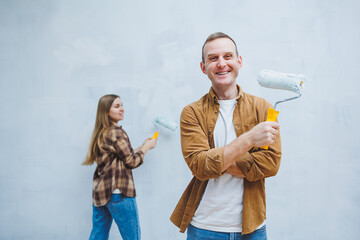 Young married couple in love in shirts and jeans doing renovations, renewing painting walls with a roller, preparing to move into a new house, selective focus