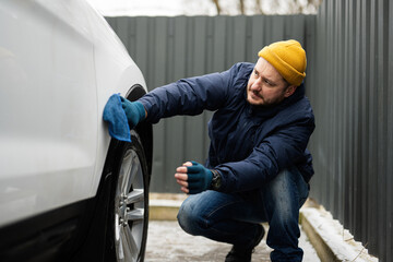 Fototapeta na wymiar Man wipes american SUV car with a microfiber cloth after washing in cold weather.