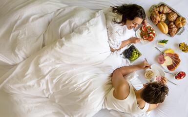 attractive, young, sexy, loving couple having romantic enjoyable breakfast in bed at home or hotel...