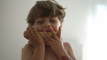 One small boy devouring yellow melon fruit indoors. Portrait face close up of little kid eating healthy snack food