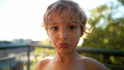 One sad little boy close up face grimacing standing outdoors. Kid feeling unhappy