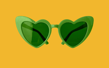 Heart-shaped green funky sun glasses on yellow background. Funny sunglasses for St Patricks day