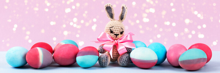 Painted Easter eggs in crimson and blue with crocheted easter bunny on a pink background with magic lights. Happy Easter concept. Banner