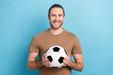 Photo of cheerful good mood man wear beige t-shirt holding football ball isolated blue color...