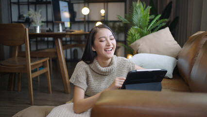 Asian woman happily using tablet to watch comedy series at home