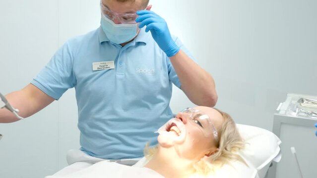 dental office doctor in blue gloves close-up corrects woman's mouth open mouth treat teeth transparent glasses to protect eyes cleaning teeth whitening treatment gums optragate mouth expander