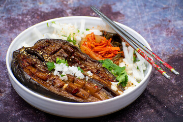 Vegan  Japanese or Korean miso grilled eggplant  with radish and pickles over rice in a white  bowl, chopsticks