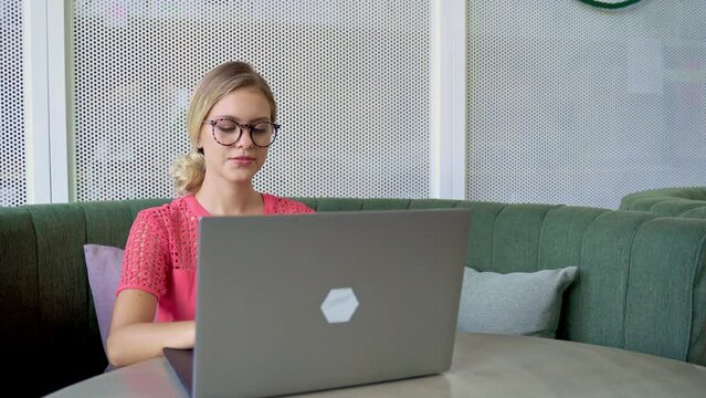 beautiful blond woman with glasses working remotely on a laptop in a coffee shop