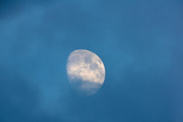 Full glowing moon closeup on blue sky and dark misty clouds