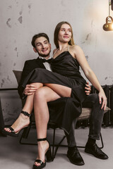 A happy young couple in elegant clothing. The girl is sitting on her boyfriend's lap against the background of an industrial room.