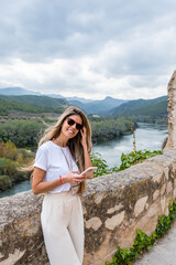 Caucasian woman with long blonde hair with her smartphone supported on the wall near de river in the village