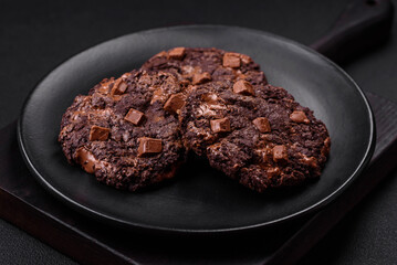 Delicious fresh oatmeal round cookies with chocolate on a black ceramic plate