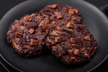 Delicious fresh oatmeal round cookies with chocolate on a black ceramic plate