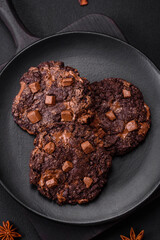 Delicious fresh oatmeal round cookies with chocolate on a black ceramic plate