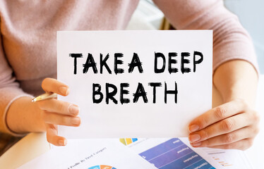 A girl in light clothes with a sign in her hands sits at the table. Lettering TAKE A DEEP BREATH. Content lettering corresponds to business concept.