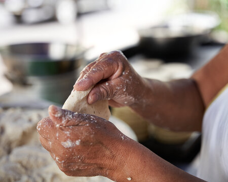 Unrecognizable elderly woman preparing corn tortillas by hand on a griddle in her modest street kitchen