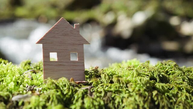A flat wooden model of a house in a natural environment. Healthy living background with blurred sunny light.