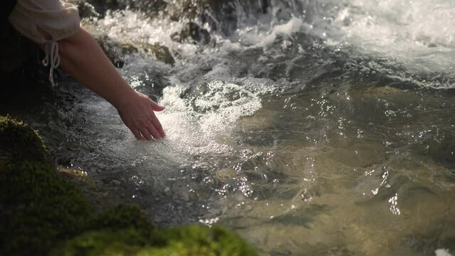 A woman's hand is playing and scooping water in a clean river. Hand holding and pouring fresh water. Slow motion.
