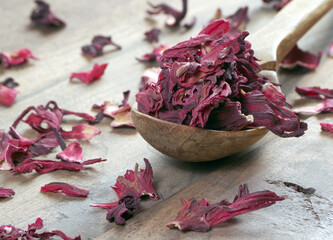 dry hibiscus in a wooden spoon. dried hibiscus petals on a wooden table. hibiscus tea.  © Oleksii