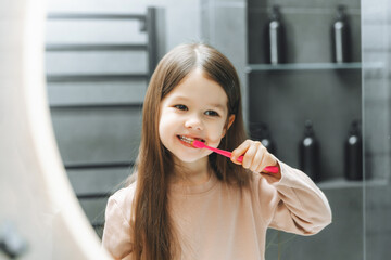 Happy little girl brushing her teeth in front of a bathroom mirror. Morning hygiene.