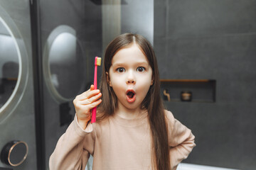 Happy little girl brushing her teeth in front of a bathroom mirror. Morning hygiene.