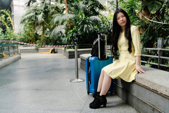 a girl with her blue suitcase and dressed in yellow at the station waiting for her means of transport