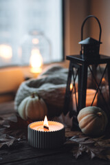 Cozy autumn composition with aromatic candle, pumpkins, wool sweater, leaves, cinnamon. Aromatherapy on a grey fall morning, home atmosphere of cosiness and relax. Wooden background close up.