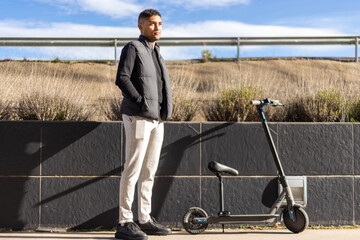 Latin man in formal wear next to an electric scooter on the sidewalk. Young latin businessman near an electric scooter.