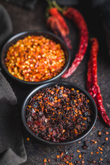 Smoked dry chili pepper flakes. Crushed red peppers in bowl on black table.