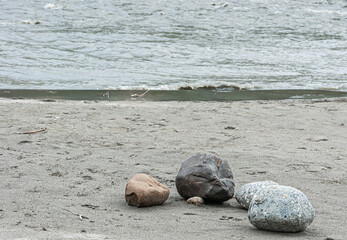 Denali Park, Alaska, USA - July 24, 2011: Nenana River. 4 smaller boulders of different colors and sizes on sandy gray shoreline. Water in back