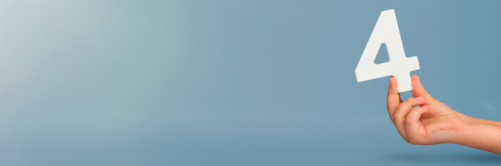 number four in hand. Hand holding white number 4 on blue background with copy space. Concept with number four. Birthday 4 years, fourth grade, four day work week