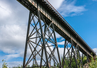Obraz premium Denali Park, Alaska, USA - July 24, 2011: Nenana River. Alaska Railroad bridge cuts diagonally through blue cloudscape with some green foliage at bottom
