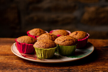 Homemade cupcakes in paper forms on wooden table on dark background.