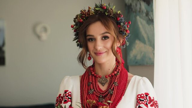 Close up Portrait of Beautiful bride dressed in ukrainian ethno clothes. Woman in a wreath of flowers standing at home. Morning of the bride concept. Medium shot