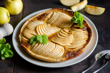 Apple french pie: temptation on black background. Traditional open pie with sliced thin parts of apples, decorated with mint leaves.