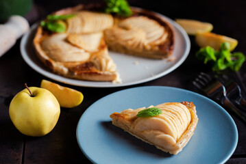 Piece of apple French pie on blue plate looks appetizing and surprisingly fresh. Thin slices of juicy apples and crispy puff pastry covered with sweet brown sugar create attractive dessert. 