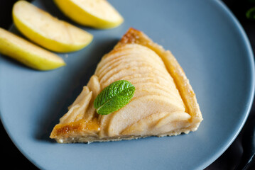 Piece of apple French pie on blue plate looks appetizing and surprisingly fresh. Thin slices of juicy apples and crispy puff pastry covered with sweet brown sugar create attractive dessert.  